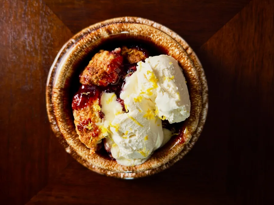 Warm peach and berry cobbler with cream and fresh lemon zest